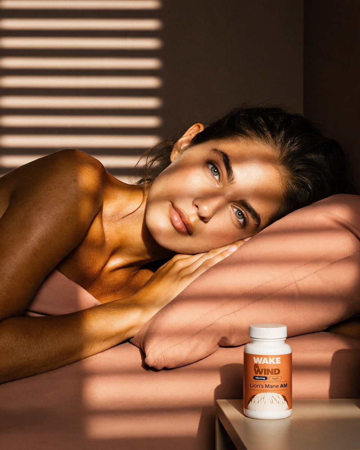 A woman waking at 06:40 in stripes of morning light, a Lion's Mane AM bottle on the nightstand
