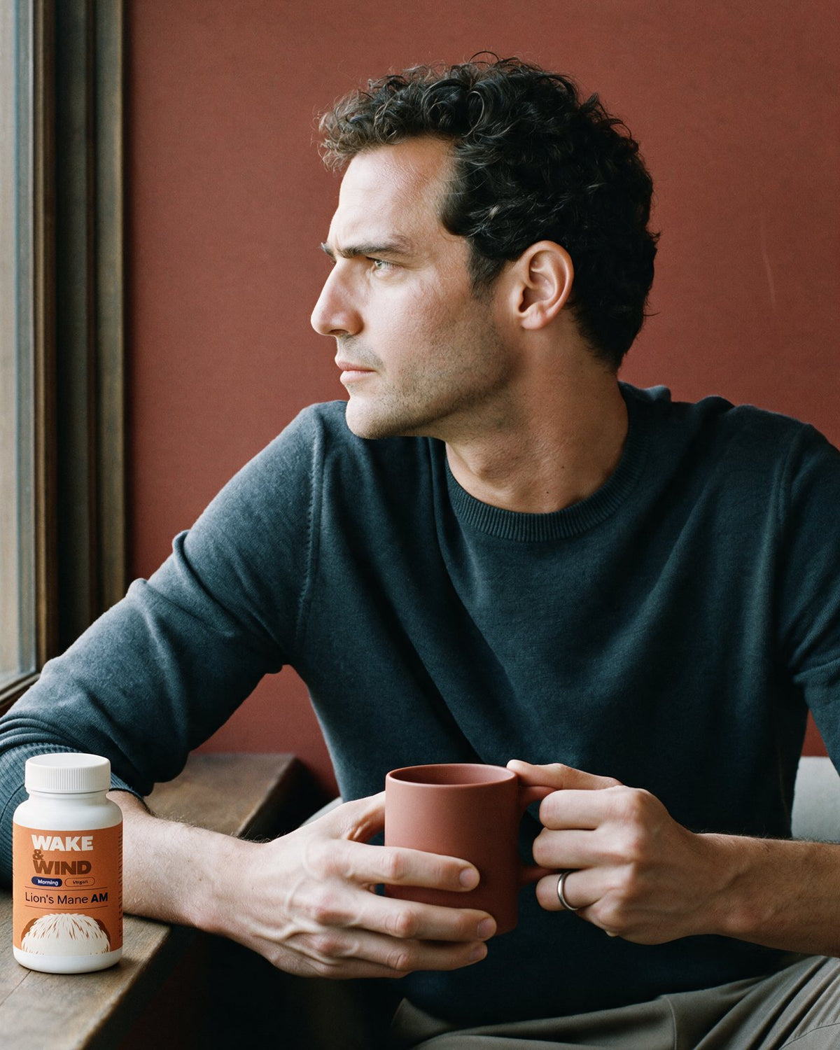 A man with his first coffee at 07:20 by the kitchen window, a Lion's Mane AM bottle beside him